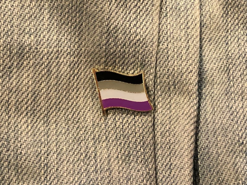 May include: Asexual pride flag pin with black, gray, white, and purple stripes. The pin is on a denim background.