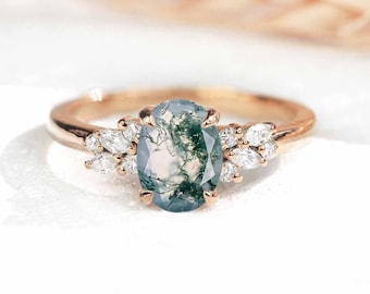 Op de afbeelding: Een ring van roségoud met een ovale moss-agaten edelsteen omringd door een cluster van kleine, ronde diamanten.