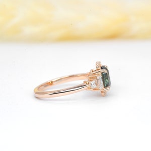 Puede incluir: Un anillo de compromiso de oro rosa con una piedra preciosa verde rodeada de diamantes m&aacute;s peque&ntilde;os.