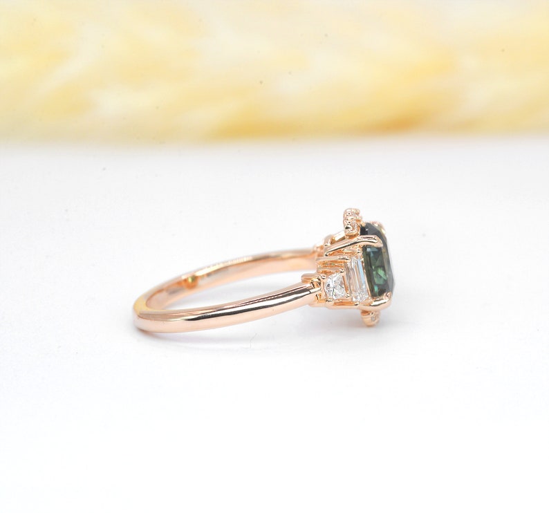 Puede incluir: Un anillo de compromiso de oro rosa con una piedra preciosa verde rodeada de diamantes m&aacute;s peque&ntilde;os.