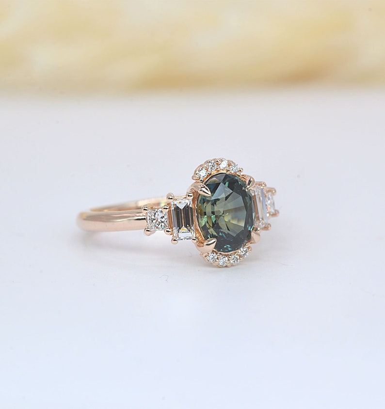 Teal sapphire and baguette diamond cluster engagement ring

 Teal sapphire 
 Approx. 8.35mm x 6.08 mm oval shape
 1.50ct


 Color G and clarity VS quality
 2 x 2mm princess cut 2 pcs
 2 x 4mm baguette cut 2pcs
 1.5mm Round brilliant-cut 8 pcs