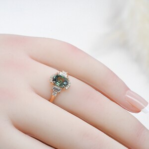 Puede incluir: Un anillo de oro con una piedra ovalada verde rodeada de diamantes m&aacute;s peque&ntilde;os. El anillo est&aacute; puesto en un dedo de maniqu&iacute;.