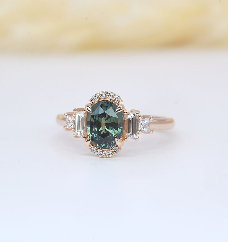 teal sapphire diamond cluster ring

 Teal sapphire 
 Approx. 8.35mm x 6.08 mm oval shape
 1.50ct


 Color G and clarity VS quality
 2 x 2mm princess cut 2 pcs
 2 x 4mm baguette cut 2pcs
 1.5mm Round brilliant-cut 8 pcs