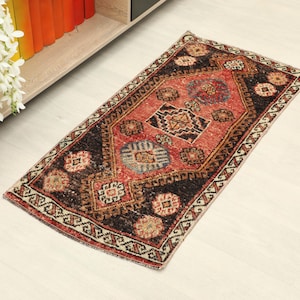 May include: A rectangular, vintage-style rug with a central medallion design. The rug features a red and black color palette with intricate patterns and borders. The rug is placed on a light-colored wooden floor.