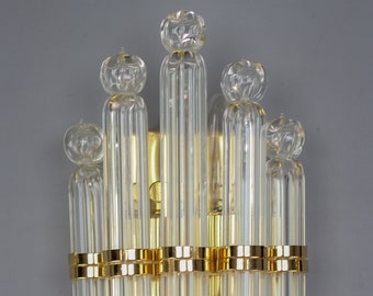 May include: A gold and clear glass wall sconce with a geometric design. The sconce has multiple clear glass tubes with rounded ends and a gold metal band around the center.