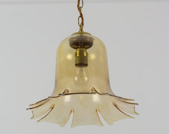 May include: A brass and amber glass pendant light fixture with a chain hanging from the ceiling. The glass shade has a bell shape with a scalloped edge.