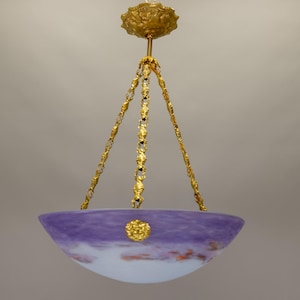 May include: A vintage chandelier with a purple and white glass bowl shade. The shade is suspended by ornate gold chains and a decorative ceiling mount. A gold emblem adorns the center of the shade.