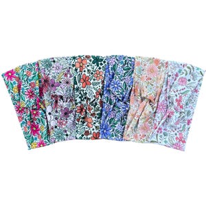 May include: A collection of floral headbands in various colors. Each headband features a different floral pattern, including pink, purple, orange, and blue flowers on a white background. The headbands are made of soft fabric and are designed to be comfortable to wear.