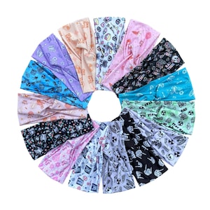May include: A collection of fifteen fabric headbands arranged in a circle, featuring various patterns including skeletons, skulls, flowers, and radiation symbols with text such as X-Ray Tech and Stay Rad in colors like pink, blue, black, and white.