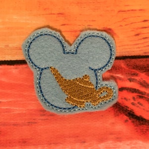 May include: A blue felt patch with a gold embroidered genie lamp inside a Mickey Mouse head shape.