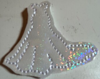 May include: A white fabric applique with a sparkly iridescent finish and a white stitched design. The applique is shaped like a bell.