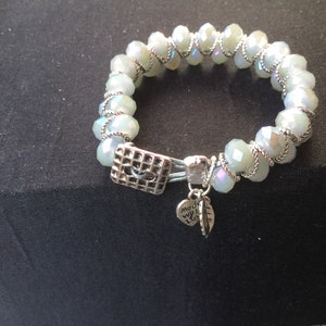 May include: A silver bracelet with white iridescent beads and a silver charm that says "Made with Love".