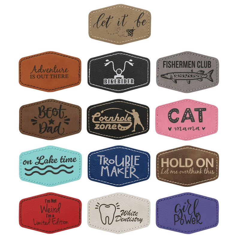 May include: Twelve different leather patches with various sayings and designs. The patches are brown, black, gray, blue, pink, white, and purple. Some of the sayings include "Let it be", "Adventure is out there", "Best Dad", "Cornhole Zone", "Cat Mama", "Trouble Maker", "Hold On", "I'm Not Weird I'm a Limited Edition", "White Dentistry", and "Girl Power".
