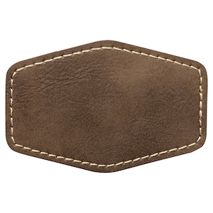 May include: A brown leather patch with a stitched border. The patch is diamond-shaped with rounded corners and a textured surface. The stitching is a light beige colour, contrasting with the darker brown leather.