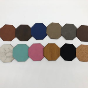 May include: A set of 12 octagonal coasters in various colours and materials, including brown leather, blue, grey, white marble, light blue, pink, wood, black, and cork.