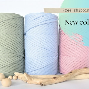 May include: Three spools of cotton rope in green, light blue, and pink. The spools are arranged in a row on a white surface with wooden beads and driftwood.