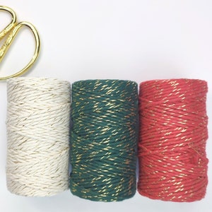 Könnte beinhalten: Drei Spulen Garn mit goldenen Akzenten. Das Garn ist weiß, grün und rot. Eine goldene Schere befindet sich in der oberen linken Ecke des Bildes.