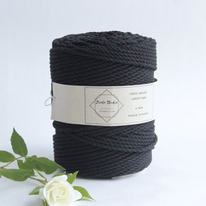 Może przedstawiać: Szpula czarnego sznurka bawełnianego, naturalnego, o grubości 4 mm, trójżyłowego. Etykieta zawiera napis "Dorte Studio" oraz "100% naturalny sznurek bawełniany 4 mm trójżyłowy".