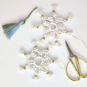 May include: Two white crocheted snowflakes with gold tassels, a pair of gold scissors, and a blue and green tassel.