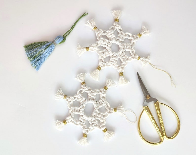 May include: Two white crocheted snowflakes with gold tassels, a pair of gold scissors, and a blue and green tassel.