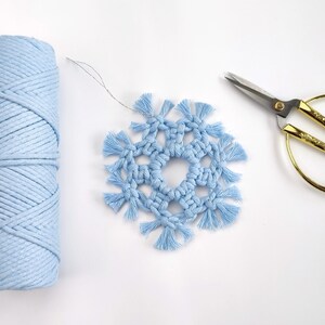 May include: A light blue macrame snowflake ornament with a spool of light blue cord and gold scissors.