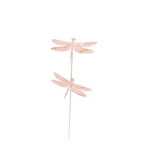 May include: Two pink metal dragonfly silhouettes on a single stem. The dragonflies are facing opposite directions.