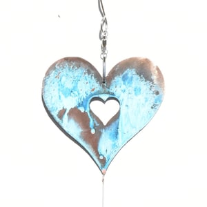 May include: A metal wind chime with three blue and brown heart-shaped ornaments hanging from a silver chain. A clear crystal prism hangs from the bottom of the chime.