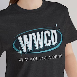 May include: Dark gray t-shirt with the text "WWCD" in a teal and white oval design, with the words "WHAT WOULD CLAUDE DO?" below. The shirt is short-sleeved and made of a soft material.