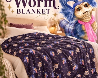 May include: A dark purple blanket featuring a repeating pattern of a blue worm character with a pink scarf and tea cups, accented by gold stars and crescent moons. The text Worm Blanket is displayed in dark purple script above the blanket.