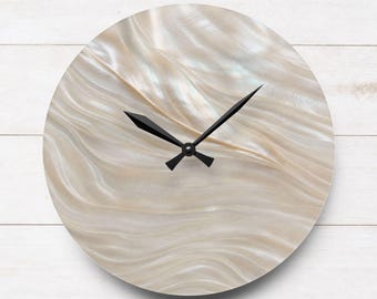 May include: A round wall clock featuring a face with a shimmering, iridescent mother-of-pearl finish displaying flowing, wavy patterns in shades of cream and off-white. The clock has two sharp, black metal hands centered on the dial.