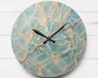 May include: A circular wall clock featuring a light blue and white marbled stone pattern with gold-toned veining throughout the face. The clock has two black pointed hands centered on the dial, indicating the time without any numerical markers.