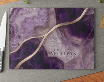 May include: A rectangular glass cutting board featuring a purple and white agate stone pattern with a gold-colored vein running across the surface. The text THE WHITLEYS EST. 2026 is printed in a dark gray serif font on the lower right side.