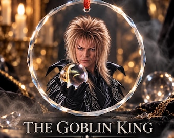 May include: A circular, faceted glass ornament featuring a portrait of a person with spiky blonde hair, wearing a black leather-style jacket and gloves, holding a crystal ball. The text reads THE GOBLIN KING and A little fantasy magic for your tree.
