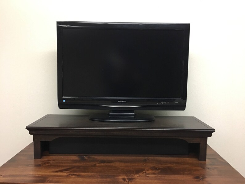 May include: A dark brown wooden TV stand with a black shelf for a sound bar. A black flat screen TV sits on top of the stand.