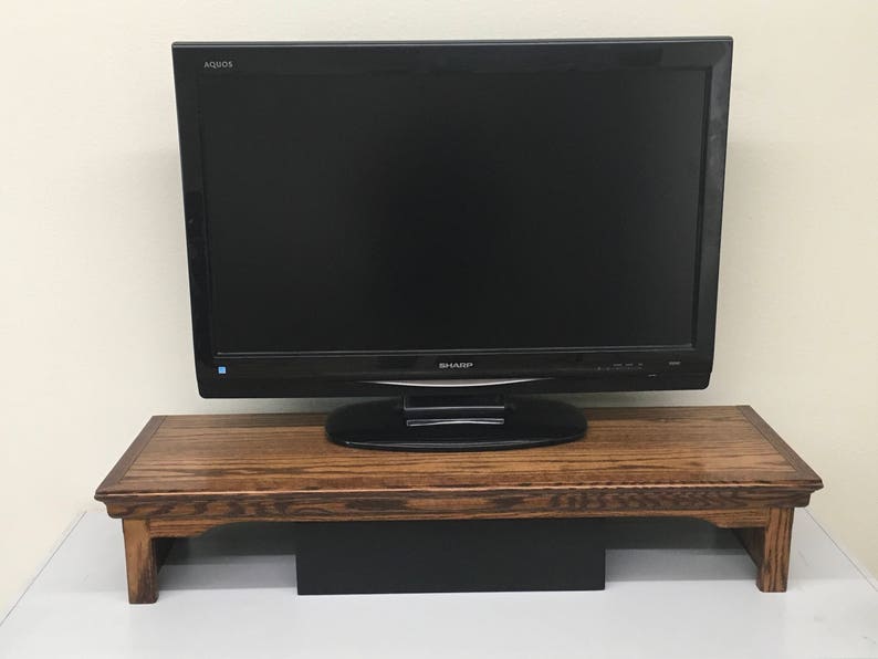 May include: A black Sharp Aquos flat-screen television sits on a rectangular wooden monitor stand. The stand features a dark brown wood grain finish with a decorative edge and four sturdy legs, providing an elevated platform for the display.