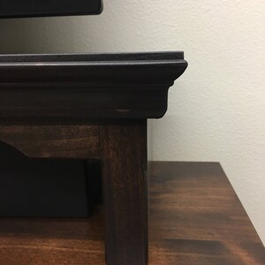 May include: A dark brown wooden TV stand with a raised edge and a simple design. The stand has four legs and is made of solid wood.