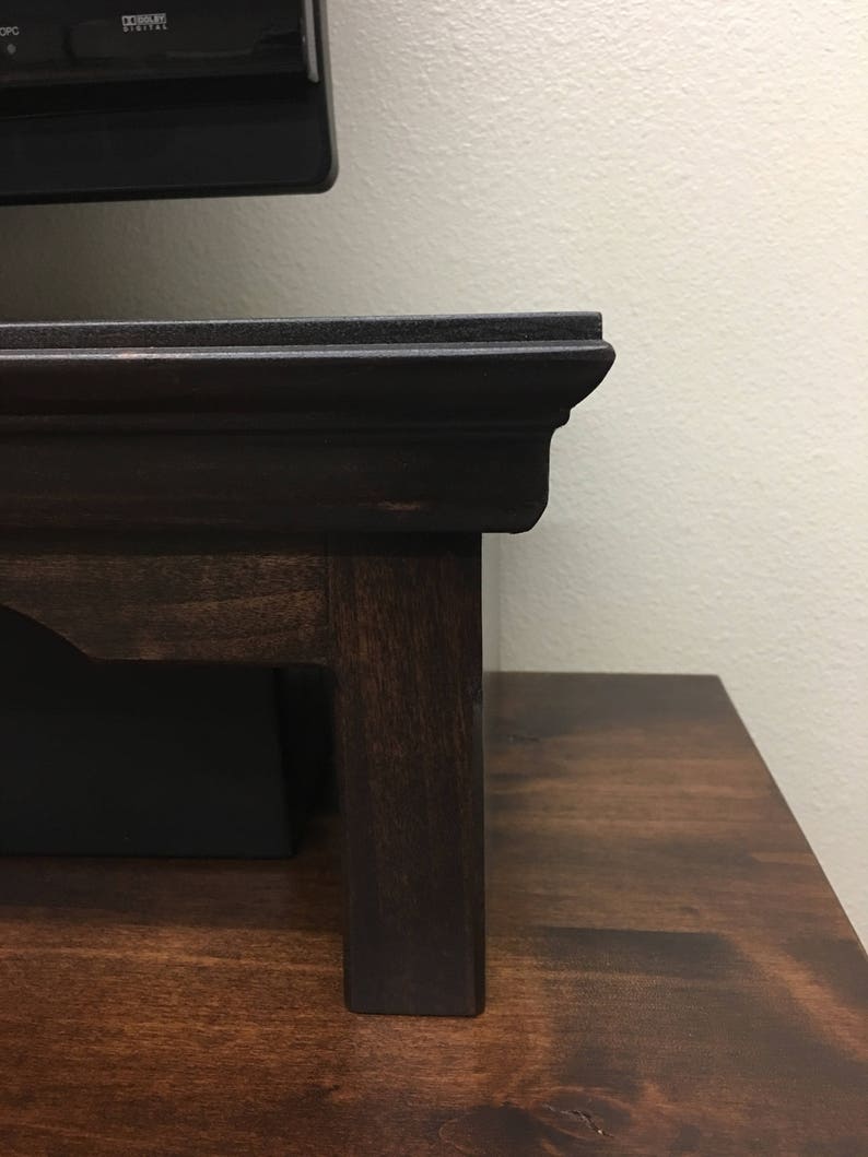 May include: A dark brown wooden TV stand with a raised edge and a simple design. The stand has four legs and is made of solid wood.