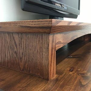 May include: A dark brown wooden TV stand with a curved bottom and a raised edge. The stand is made of solid wood and has a natural finish.