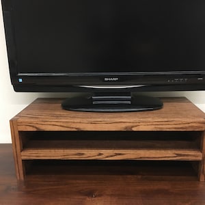 May include: A dark wood TV stand with two shelves. The stand is designed to hold a flat screen TV. A black Sharp TV is sitting on the top shelf.