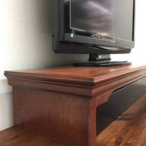 May include: A dark wood TV stand with a black drawer and a raised lip to hold a TV. The stand is made of solid wood and has a traditional design.
