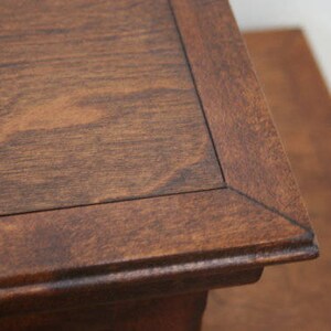 May include: A close-up of a dark brown wooden table top with a beveled edge. The table top has a natural wood grain pattern.