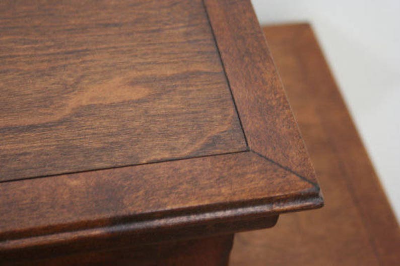 May include: A close-up of a dark brown wooden table top with a beveled edge. The table top has a natural wood grain pattern.