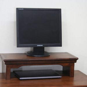 May include: A dark wood monitor stand with a laptop computer underneath and a black computer monitor on top. The monitor has the Samsung logo on the front.