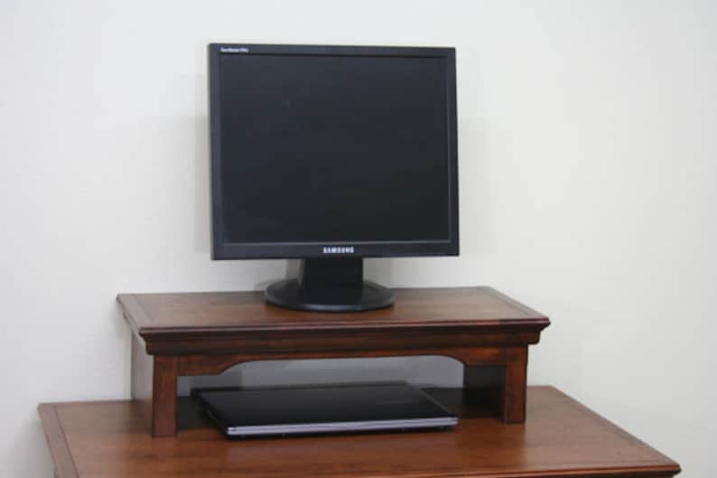 May include: A dark wood monitor stand with a laptop computer underneath and a black computer monitor on top. The monitor has the Samsung logo on the front.