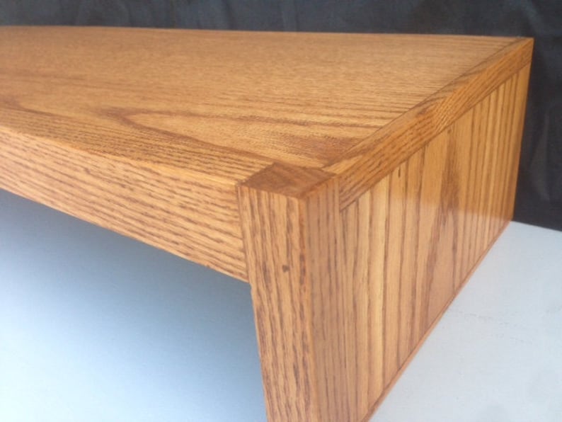 May include: A wooden shelf with a natural finish. The shelf has a simple design with a rectangular shape and a smooth surface.