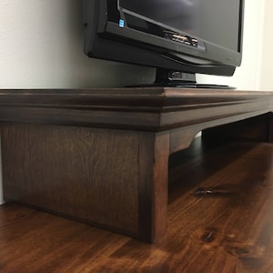 May include: A dark brown wooden TV stand with a raised edge and a shelf underneath. The stand is made of solid wood and has a simple, elegant design.