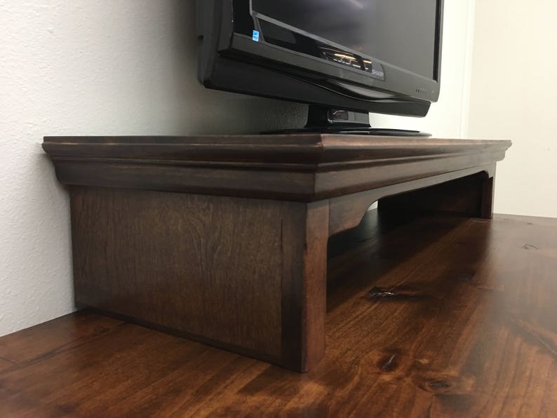 May include: A dark brown wooden TV stand with a raised edge and a shelf underneath. The stand is made of solid wood and has a simple, elegant design.