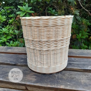 May include: A white wicker basket with a woven pattern. The basket is sitting on a wooden surface.