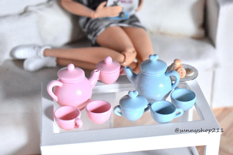 Pu&ograve; includere: Un set da t&egrave; in miniatura rosa e blu con una teiera, una zuccheriera e delle tazze. Il set da t&egrave; &egrave; su un tavolo bianco con un piano in vetro. Il set da t&egrave; &egrave; perfetto per una casa delle bambole o un set di gioco.