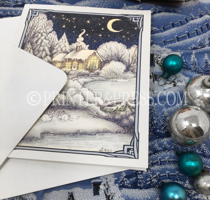May include: A snowy winter scene with a small cottage, trees, and two rabbits in the foreground. The sky is dark blue with stars and a crescent moon. The cottage has a warm glow coming from the windows. The image is framed with a decorative border.